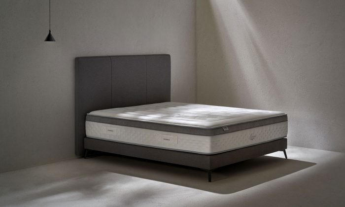 Un matelas avec Âme ressorts ensachés Springsac dont 7 zones de confort. Et tête de lit en tissu gris effet texturé.